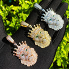 Four lion head pendants in gold, rose gold, and silver on a black glove with a green leafy background.