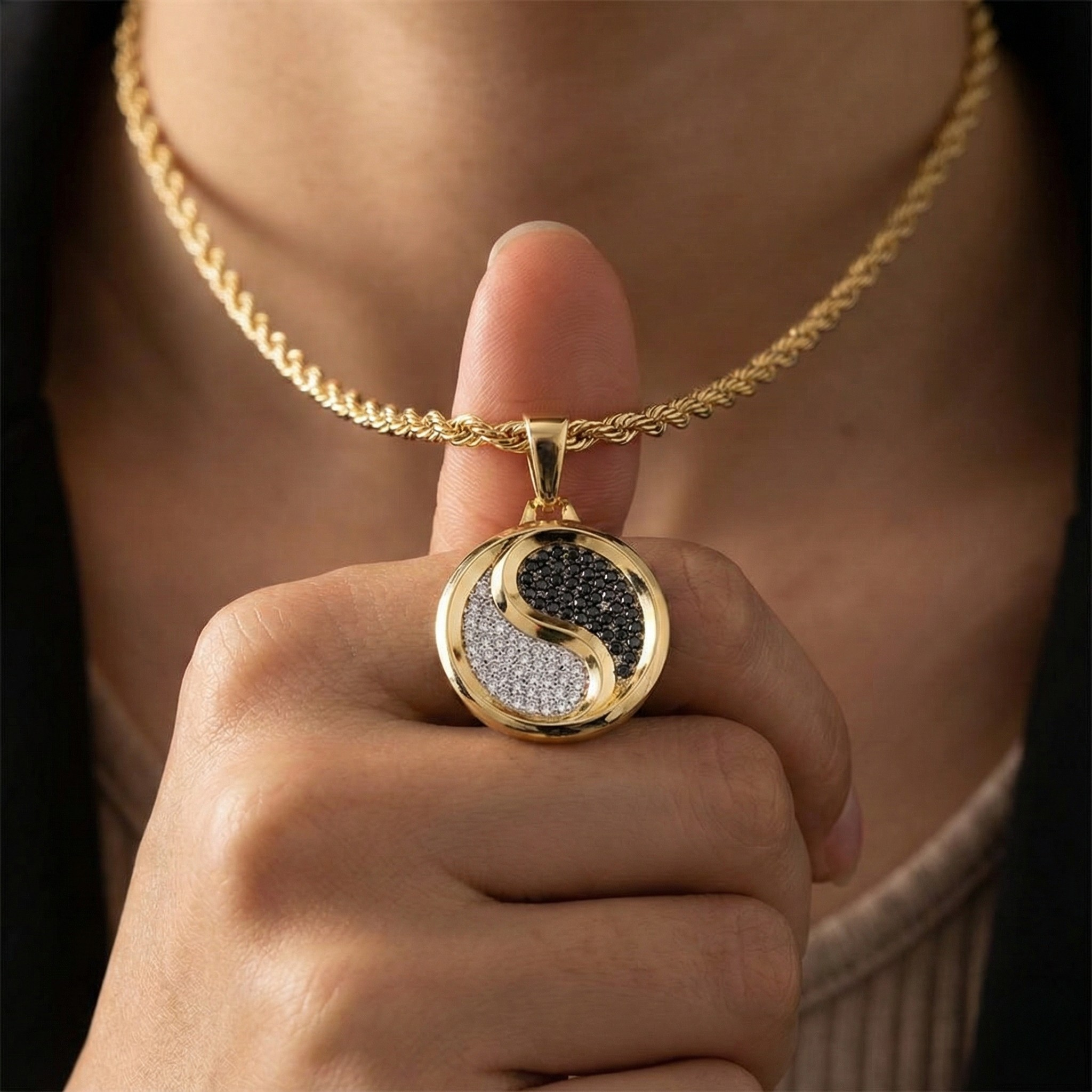 Gold necklace with a yin yang pendant held by a hand against a blurred background