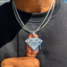 A custom gold pendant with the initials 'DC' designed in a diamond shape, being held by a person.