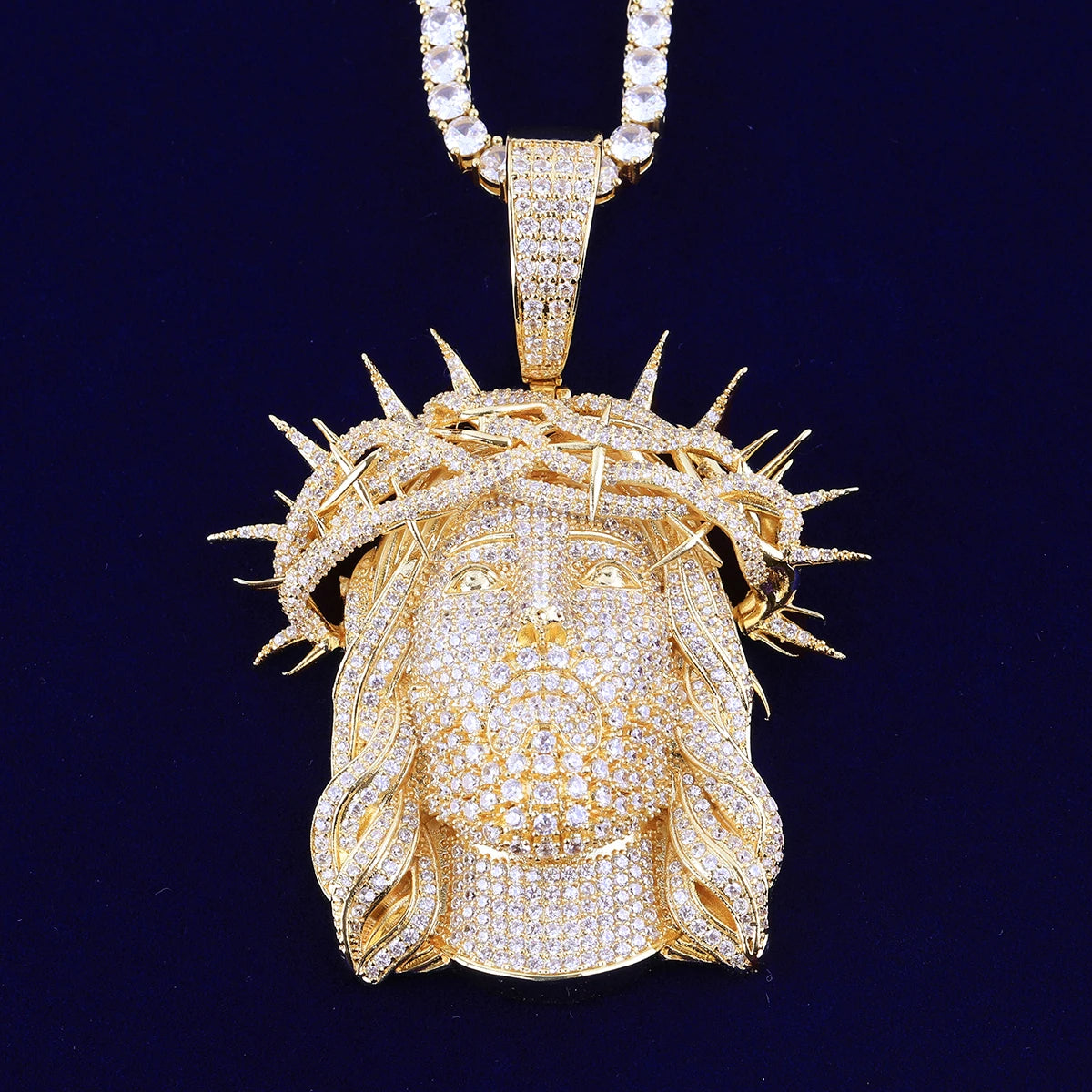 Gold pendant with a detailed face design and crown of thorns on a dark background