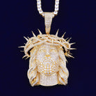 Gold pendant with a detailed face design and crown of thorns on a dark background