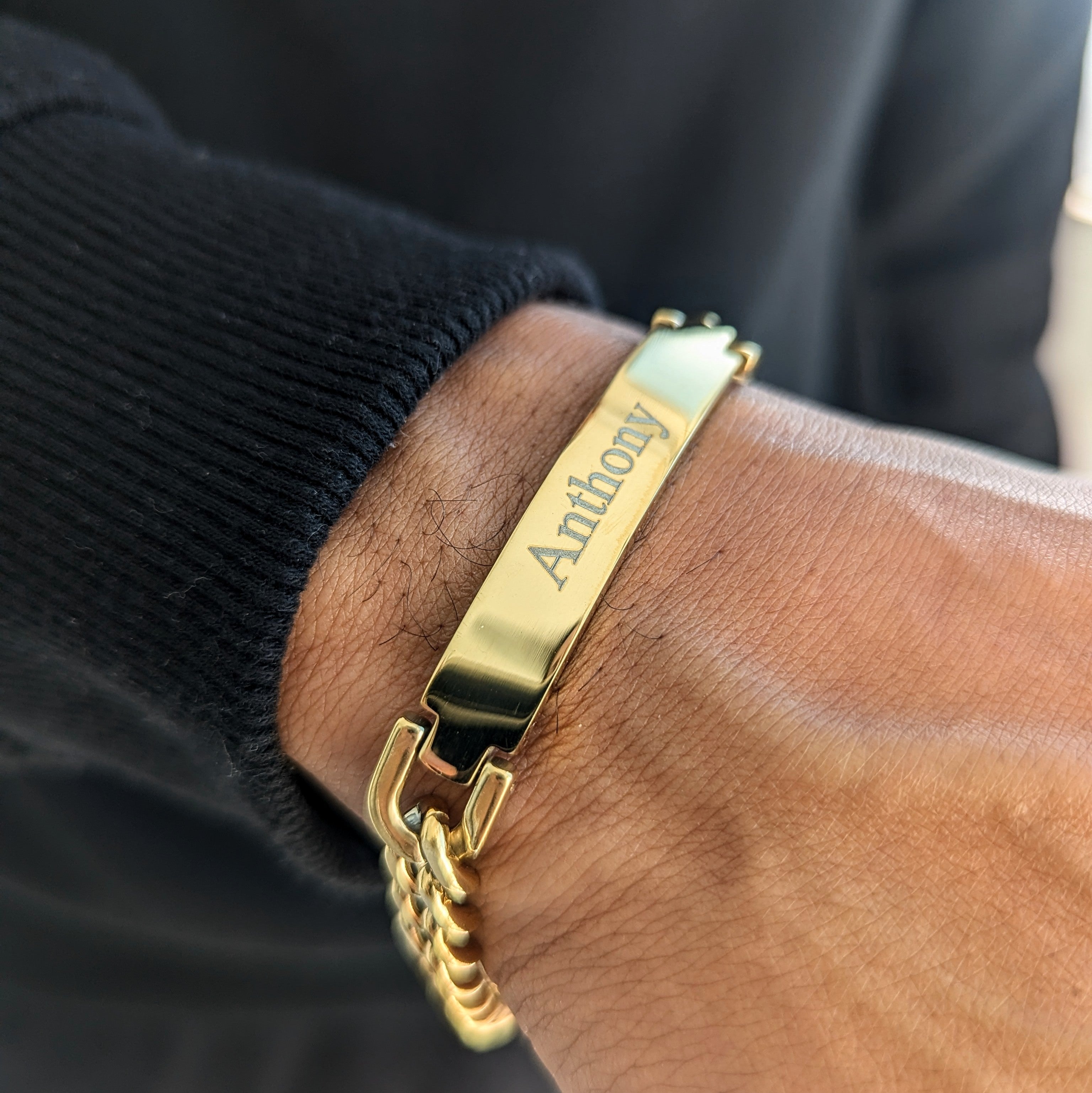 A close-up image of a person's wrist wearing a gold-plated bracelet with custom name engraving.