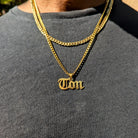 Gold chain necklace with a 'Tom' pendant on a gray shirt