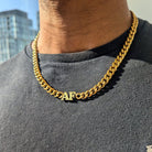 A person wearing a gray shirt and a gold Cuban link chain necklace with a custom nameplate.