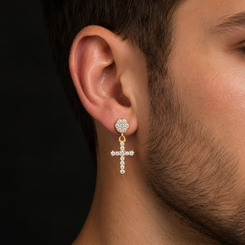 A close-up of a man's ear wearing a gold and crystal drop earring with a floral stud and a dangling cross.